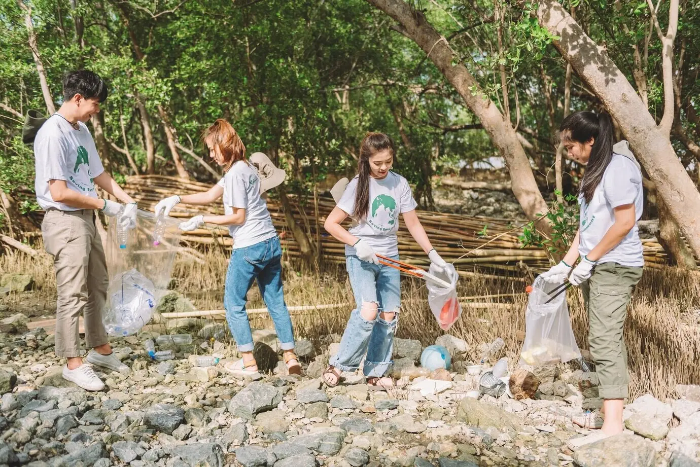 Grupo diverso de personas asiáticas voluntarias que trabajan en equipo para la conservación del medio ambiente, ayudando a recoger basura de plástico y espuma en una zona de parque; voluntariado del Día Mundial del Medio Ambiente.